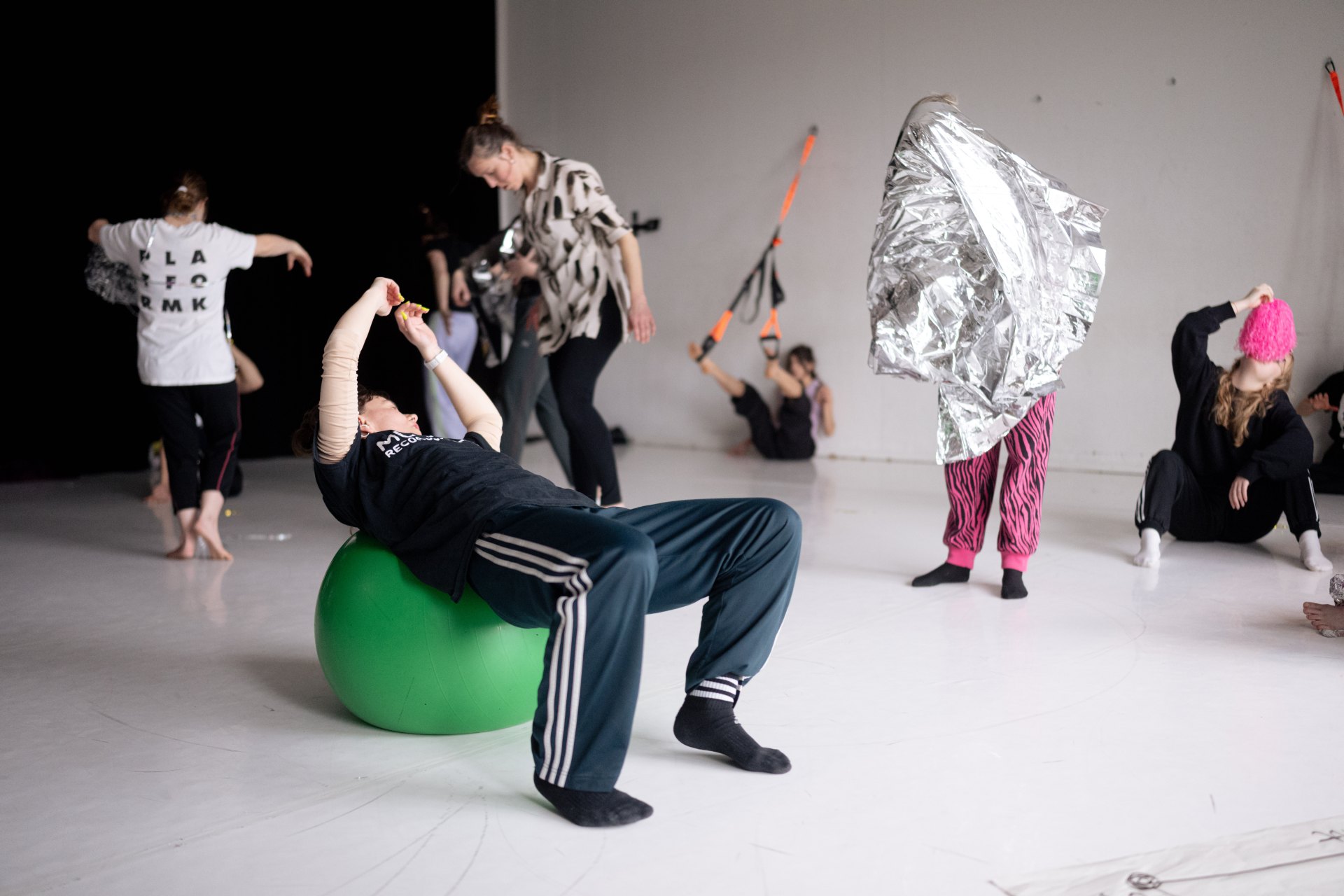 Mehrere Personen bewegen sich bei einem Workshop in einem hellen Raum mit weißem Boden. Im Vordergrund lehnt sich eine Person rücklings über einen großen grünen Gymnastikball und streckt die Arme nach oben. Im Hintergrund üben weitere Personen, wobei sich